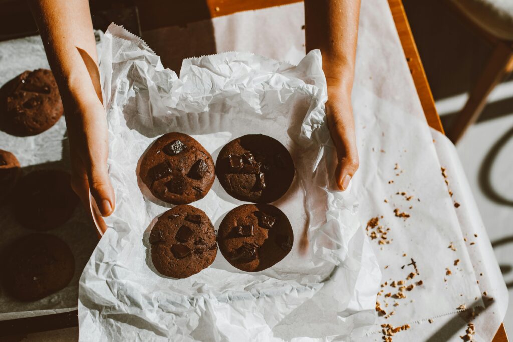 pexels photo 5846042 5846042 Delicious homemade chocolate cookies on parchment with hands holding the tray.