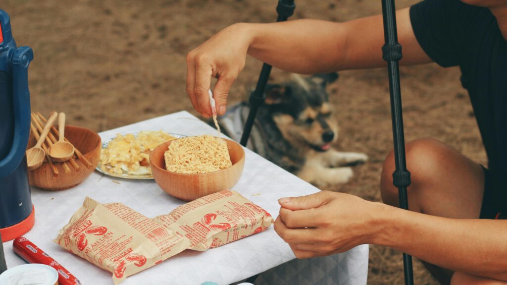pexels photo 7990284 7990284 Close-up of cooking instant noodles outdoors with a dog nearby.